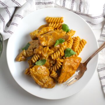 A serving of butter chicken pasta on a plate with a fork on the edge.