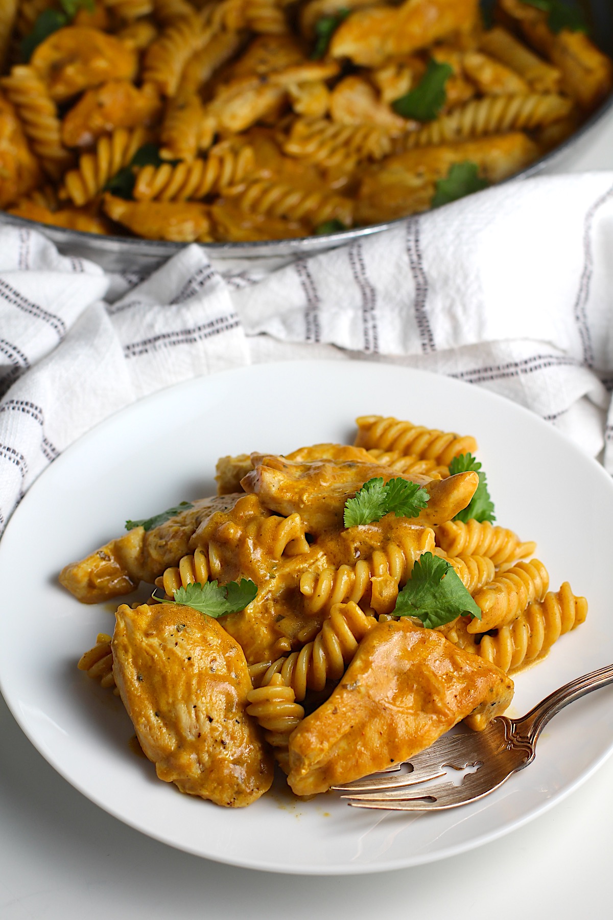 Fork resting on a plate of butter chicken pasta with cilantro garnished over the top.