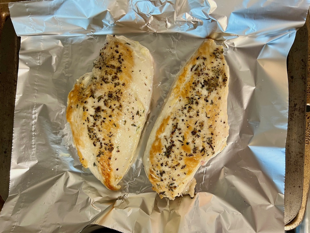 Cooked chicken breasts resting on an aluminum foil covered baking sheet.