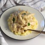 Fork resting in a creamy mixture of mashed potatoes topped with homemade chicken and gravy.