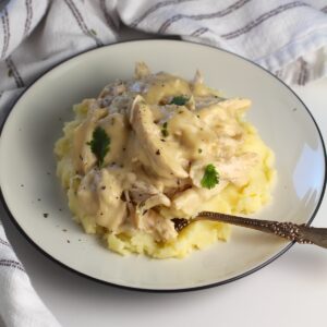 Fork resting in a creamy mixture of mashed potatoes topped with homemade chicken and gravy.