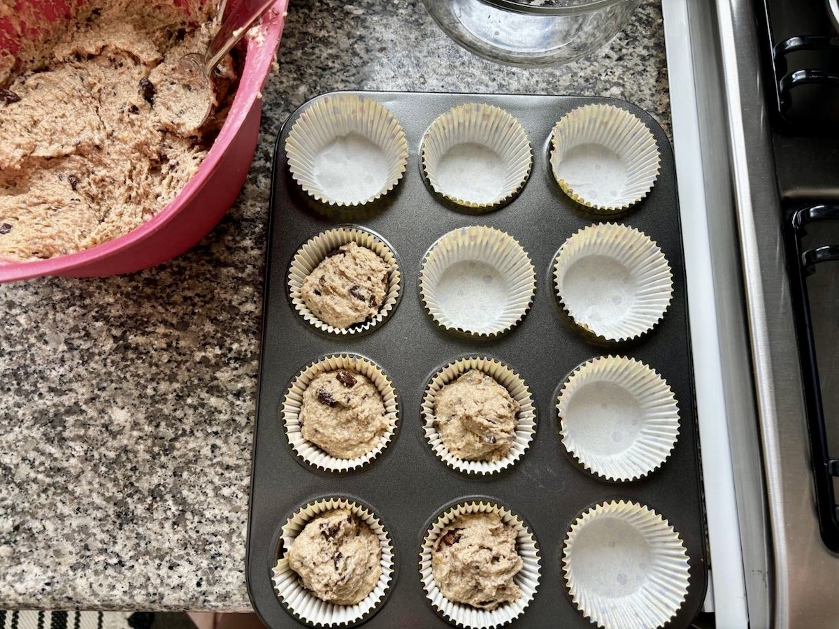 Oat banana chocolate chip muffin batter added to paper wrappers in a muffin tin, about to be placed in the oven.