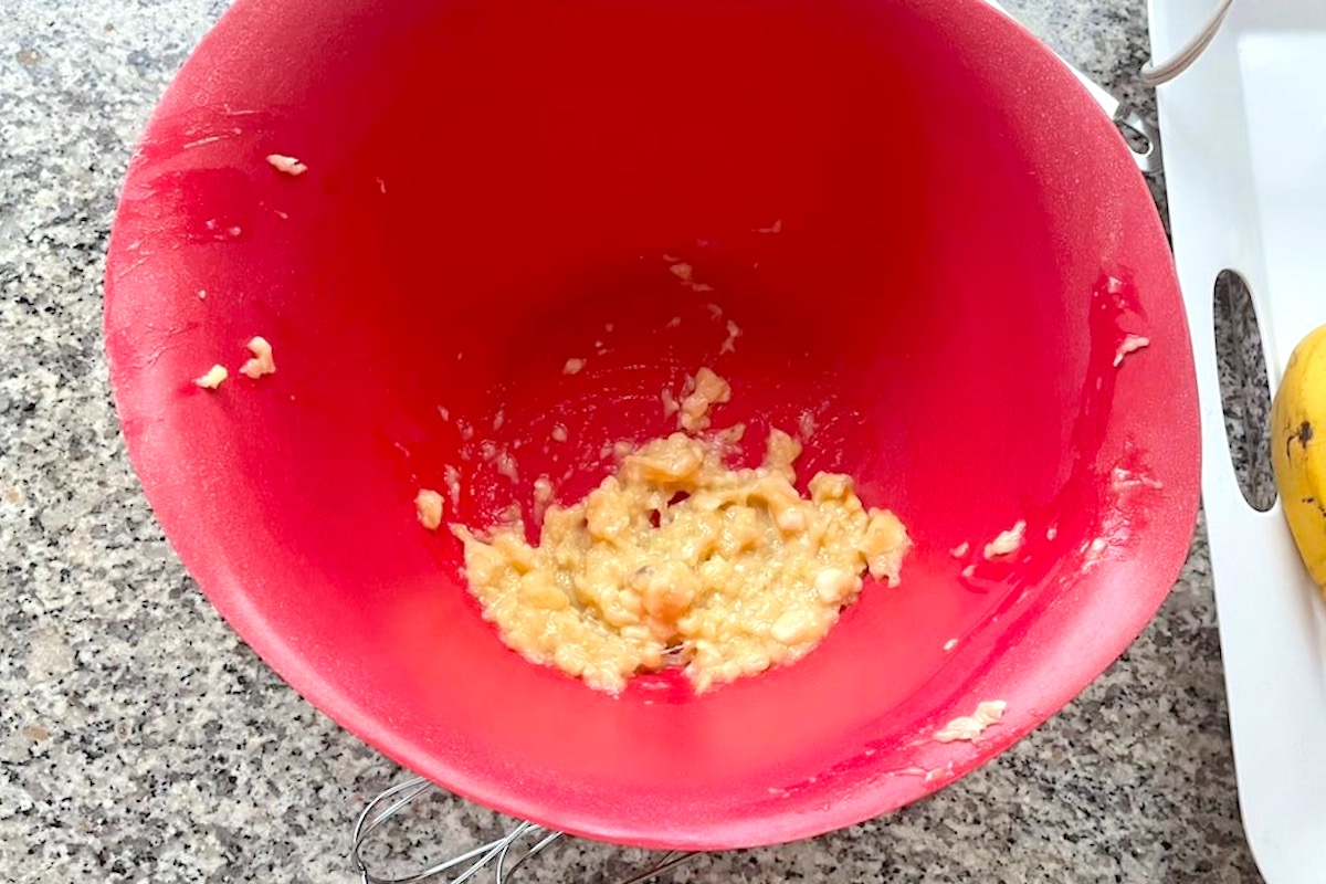 Banana mashed up in a large red bowl for the Strawberry Banana Cake recipe.