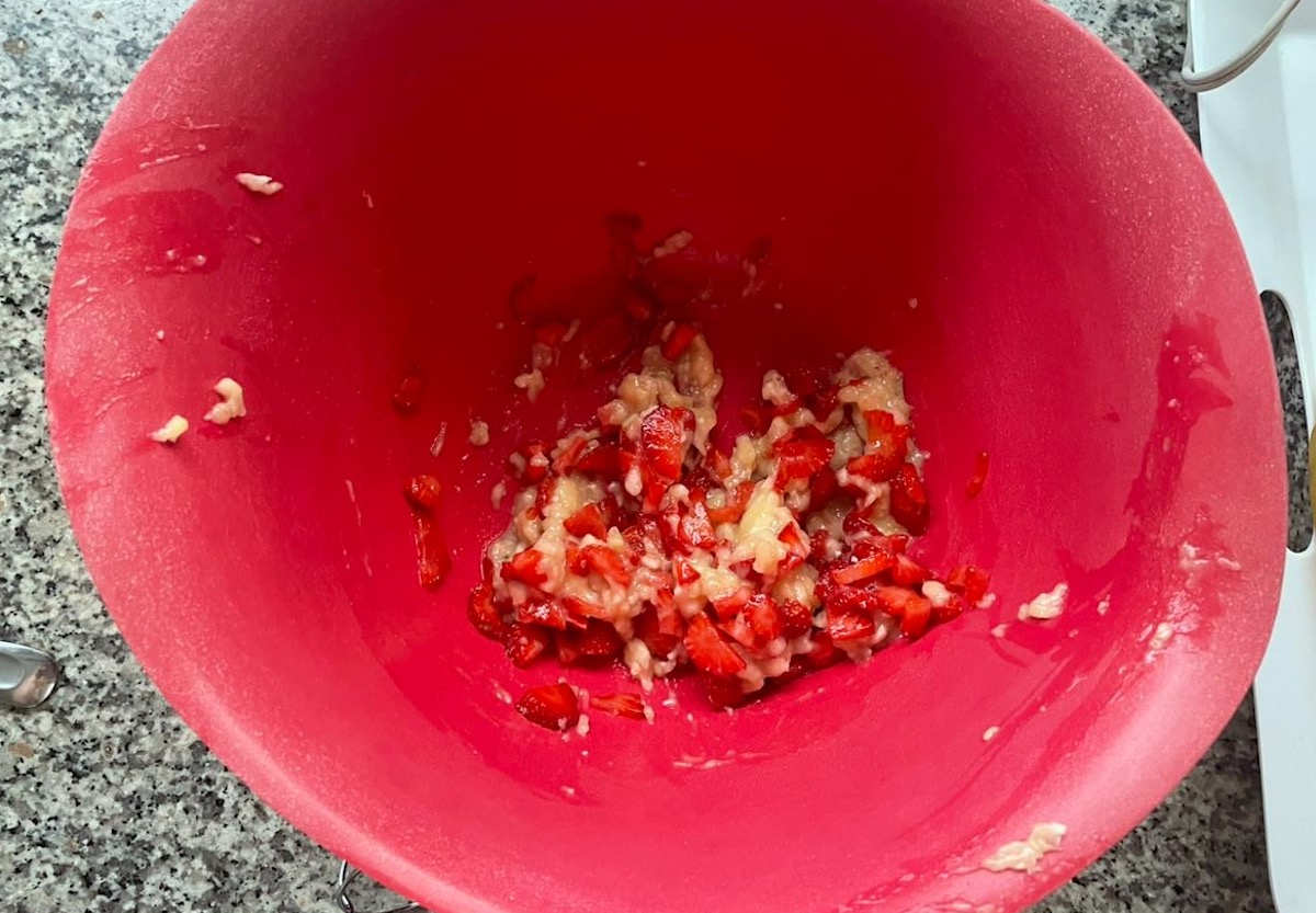 Diced strawberries mixed into the mashed banana in a large red bowl for the Strawberry Banana Cake recipe.