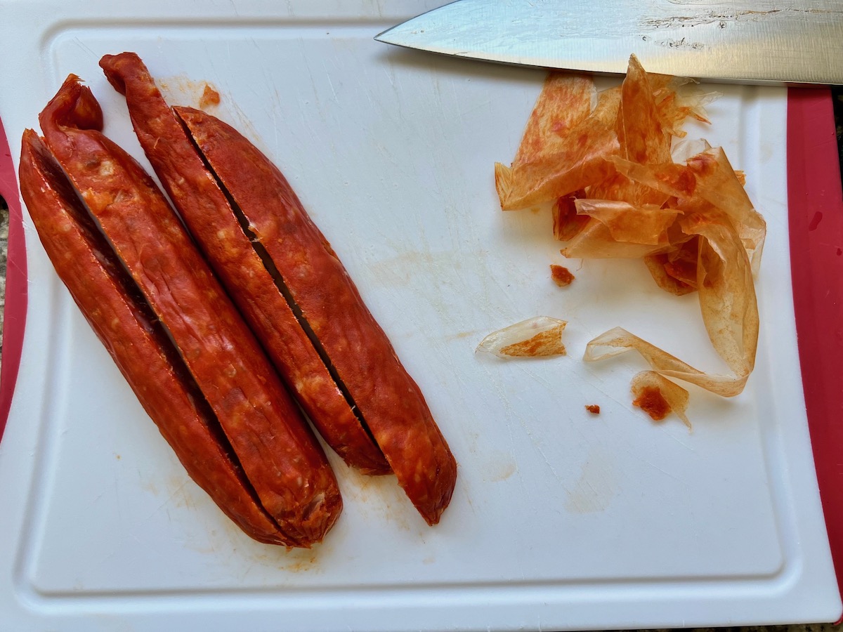 Spanish chorizo sliced into long strips before dicing on cutting board with the casing peeled off next to it and a knife for the Pasta with chorizo and chicken recipe.