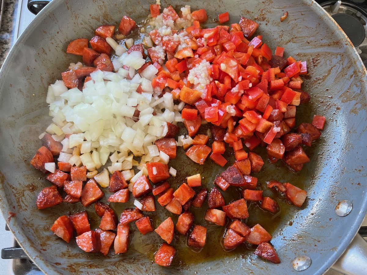 Diced red pepper, diced onion, and garlic added to the chorizo in the skillet for the Pasta with chorizo and chicken recipe.
