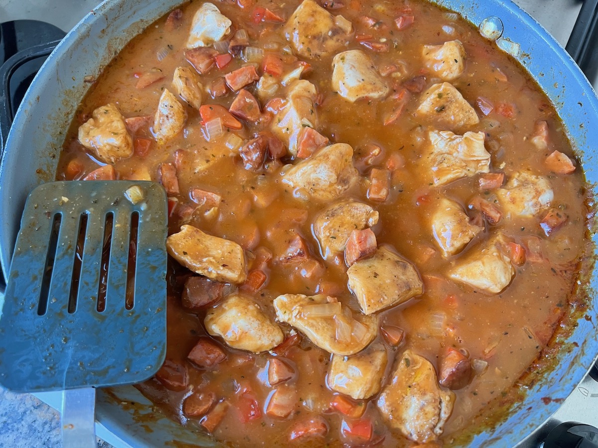 Pasta with chorizo and chicken in a skillet with the creamy sauce being stirred as it thickens.