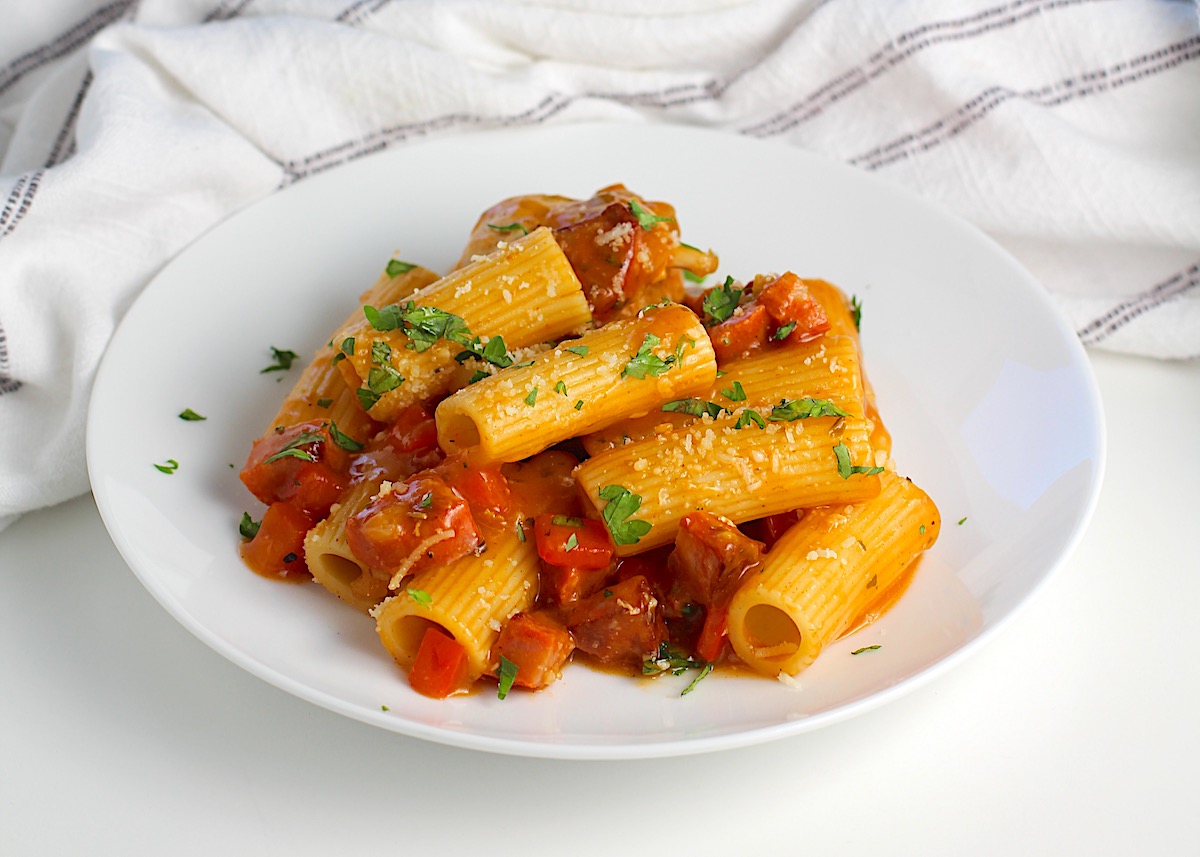 Plate of creamy coated pasta with chorizo and chicken pieces, garnished with parsley and Parmesan cheese, ready to enjoy.