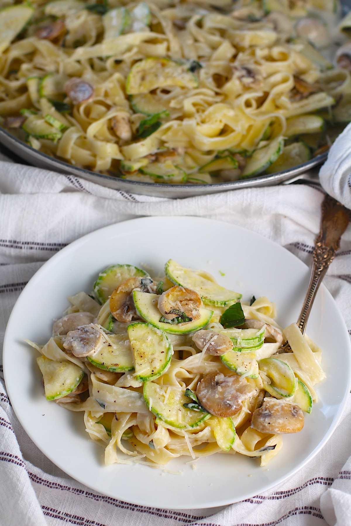 Plate of creamy pasta with zucchini and mushrooms, sprinkled with parmesan cheese with a fork resting in the mixture.