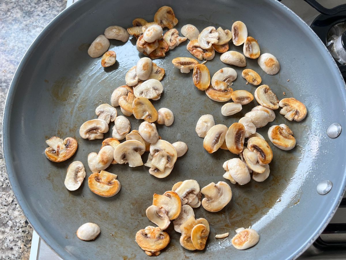 Thinly sliced mushrooms being sauteed in a skillet.