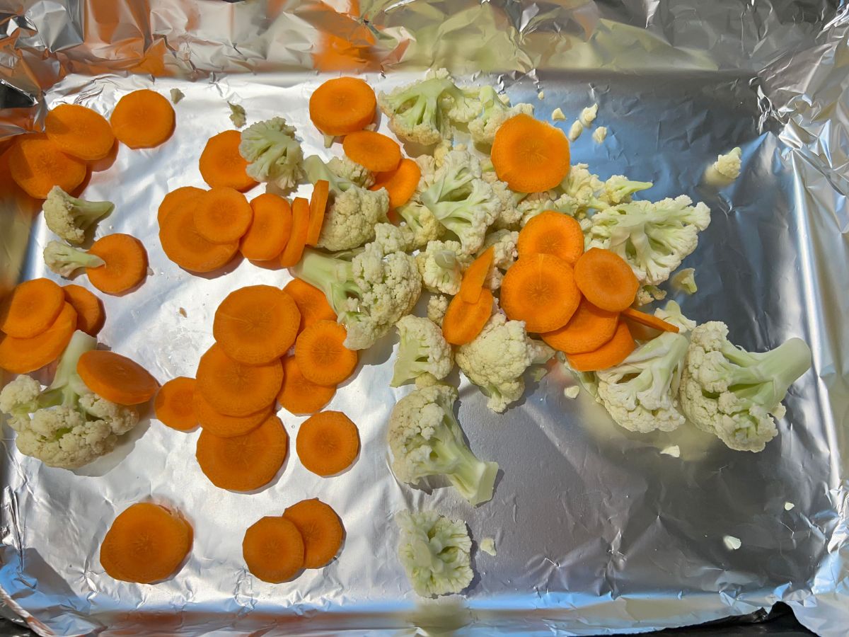 Cauliflower florets and thin sliced carrots added to an aluminum foil topped baking sheet.