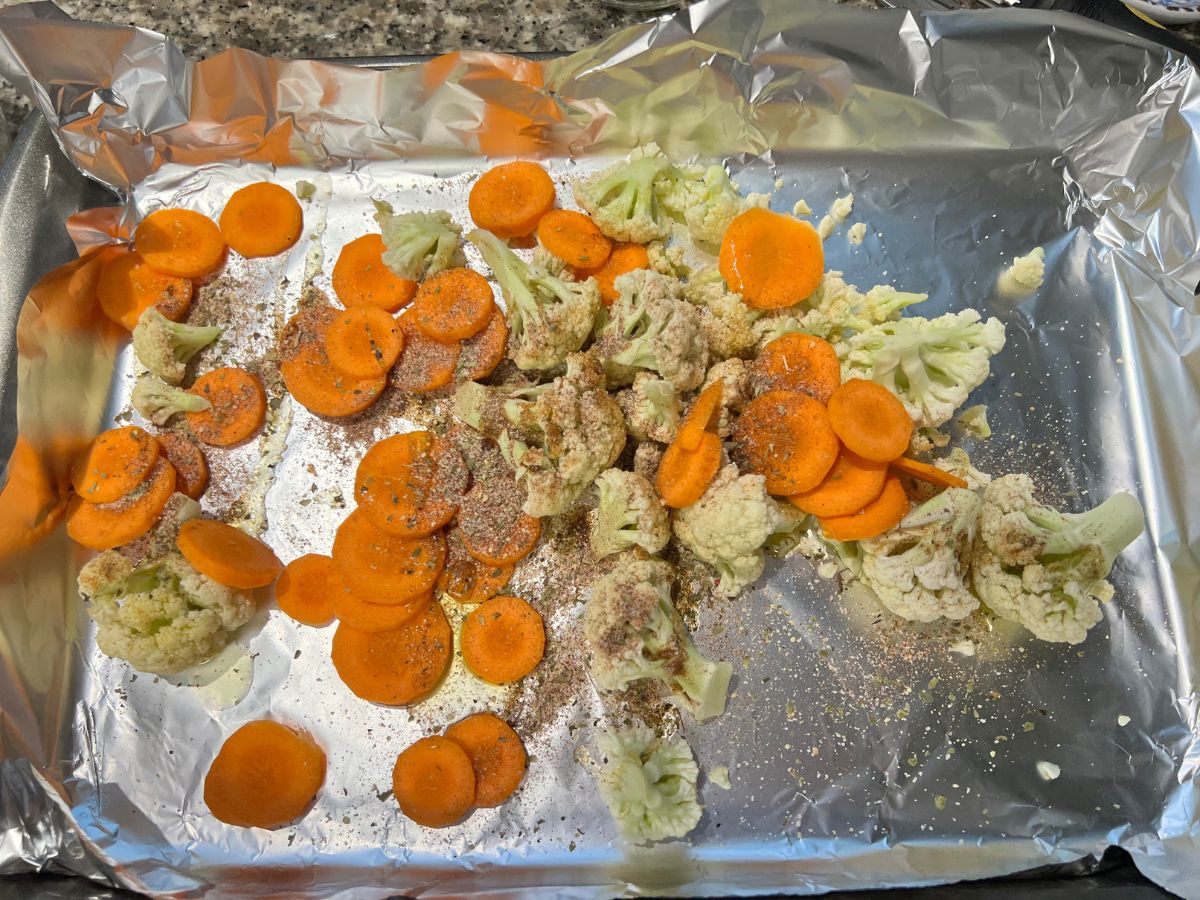 Seasonings sprinkled over cauliflower and thinly sliced carrots before baking.