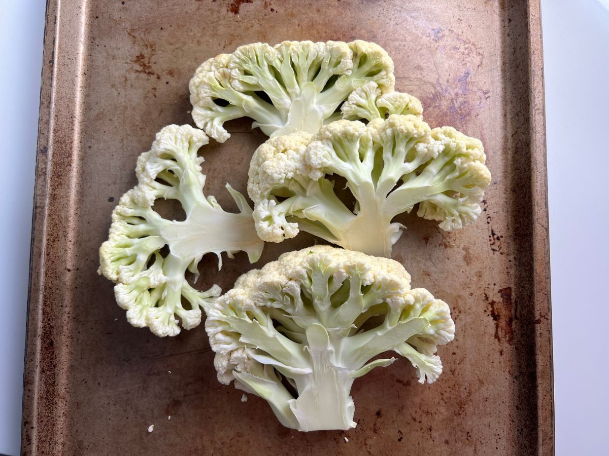 Thick cut cauliflower steaks on a baking sheet.