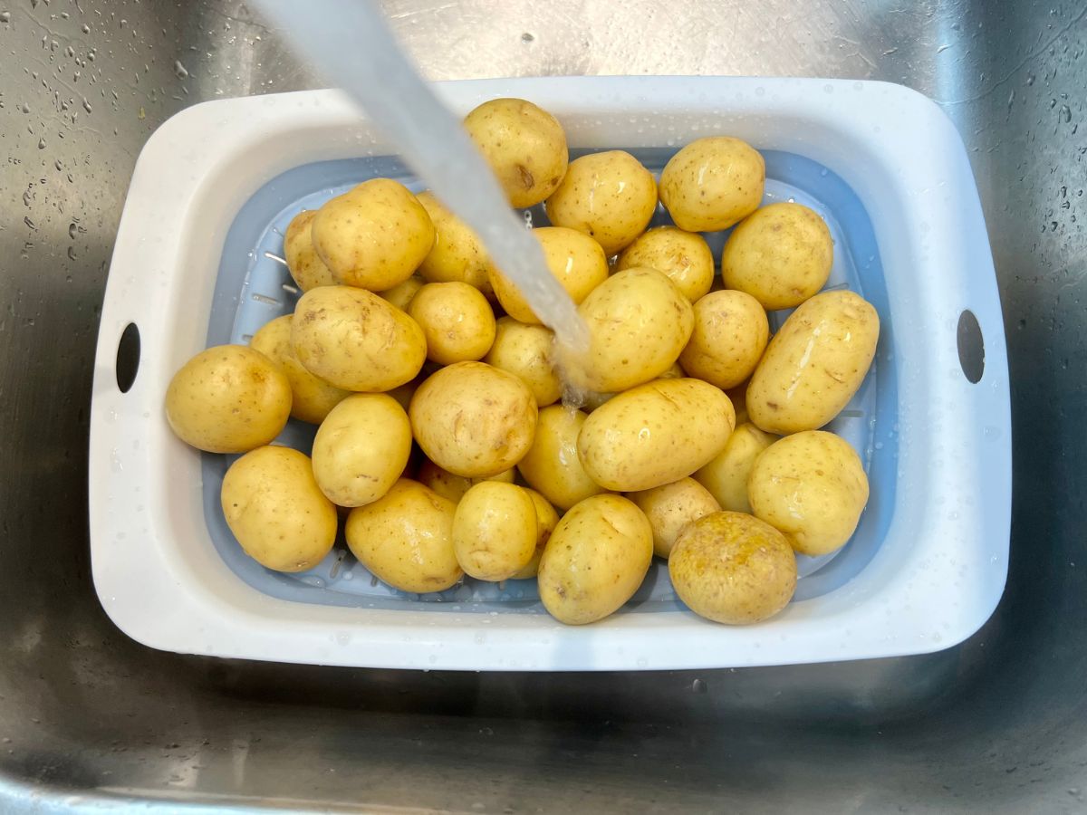 Baby potatoes in a colander being washed with a stream of water being run over them.