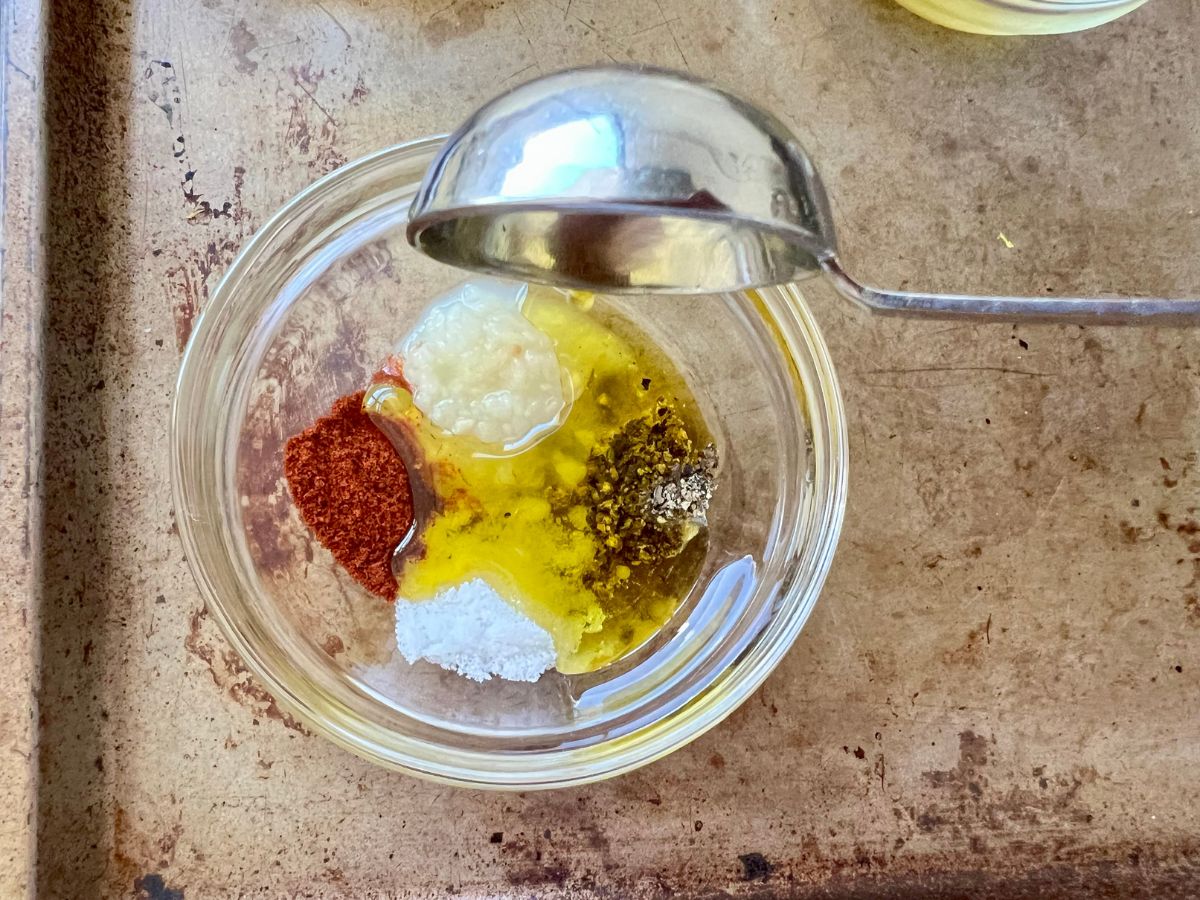 Seasonings and olive oil being added to a small dish to combine and serve over baby potatoes.