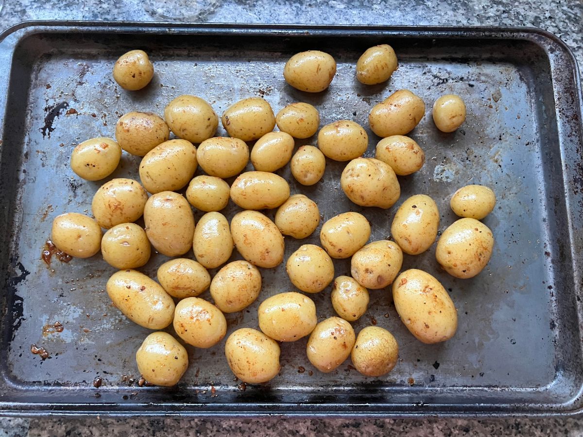 Cooked baby potatoes coated in olive oil and seasonings added to a baking sheet.