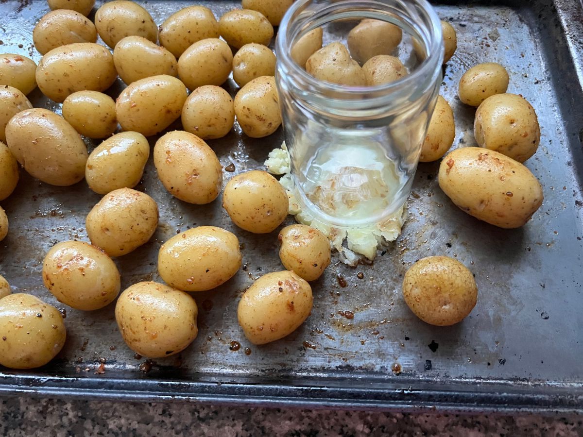 Glass jar being used to smash cooked baby potatoes on a baking sheet.