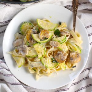 Creamy Fettuccine Pasta with Zucchini and Mushrooms and parmesan cheese shredded on top, all on a plate with a fork.