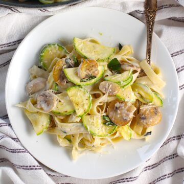 Creamy Fettuccine Pasta with Zucchini and Mushrooms and parmesan cheese shredded on top, all on a plate with a fork.