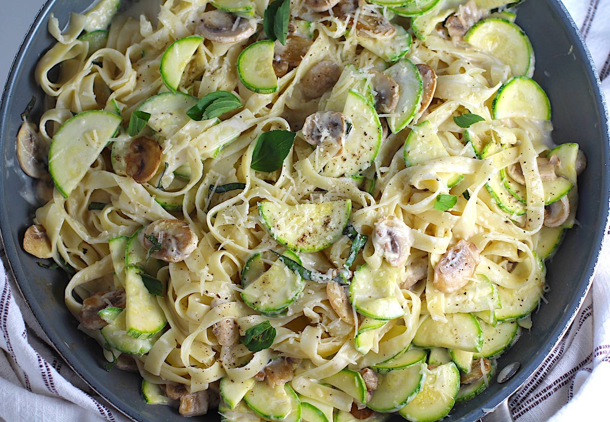 Creamy Fettuccine Pasta with Zucchini and Mushrooms in a skillet on counter with blue and white towel. Parmesan cheese is shredded on top.