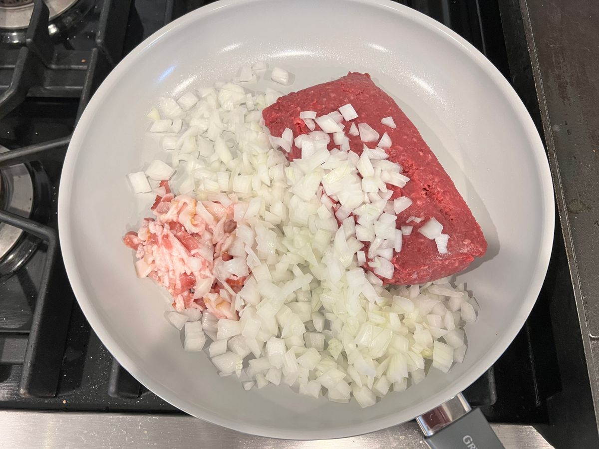 Ground beef, diced onions and chopped bacon added to a skillet.