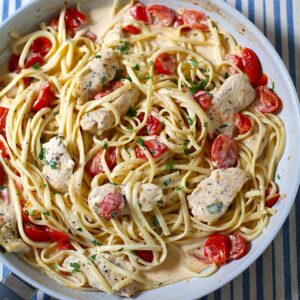 Boursin Tomato Pasta with chicken, fettuccine noodles, and cherry tomatoes in a killet on table with blue and white tablecloth.
