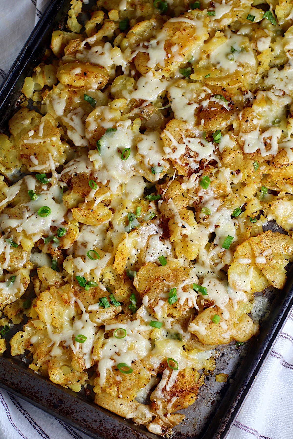 Crispy cheesy smashed potatoes recipe with everything hot on a baking sheet with sliced scallions sprinkled over.