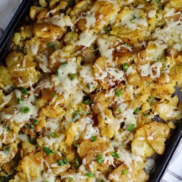 Crispy cheesy smashed potatoes recipe with everything hot on a baking sheet with sliced scallions sprinkled over.