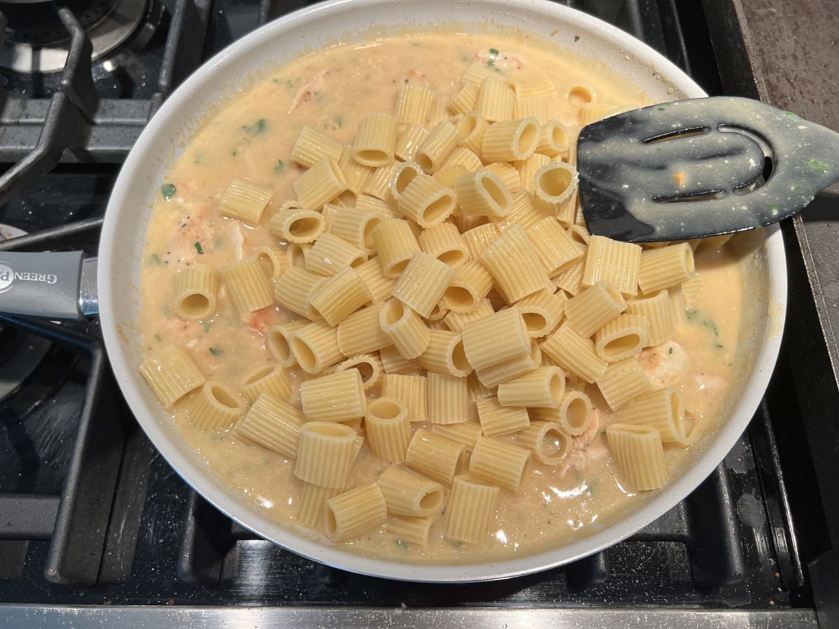 Spoon resting on the side of a skillet with the sauce coating it.