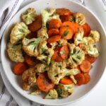 Roasted carrots and cauliflower on a plate on table next to a blue and white striped napkin.