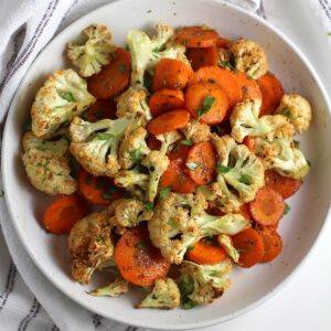 Roasted carrots and cauliflower on a plate on table next to a blue and white striped napkin.