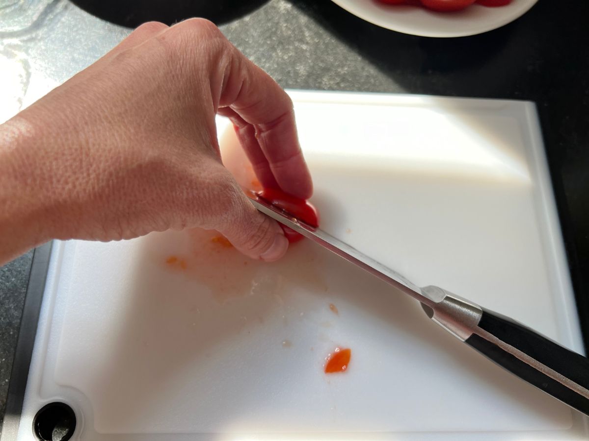 Hand using a sharp knife to slice grape tomatoes in half.