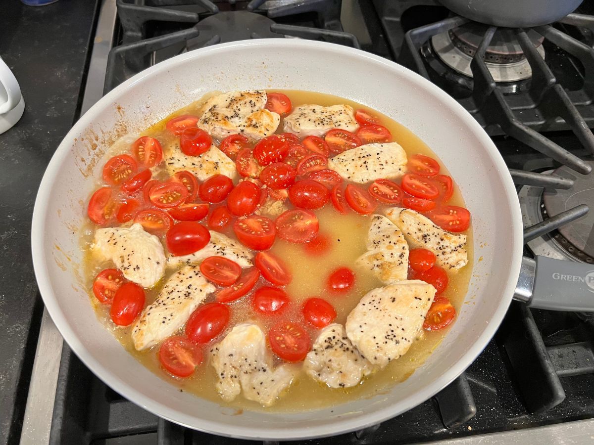 Chicken broth added to a skillet with grape tomatoes and seasoned chicken chunks.