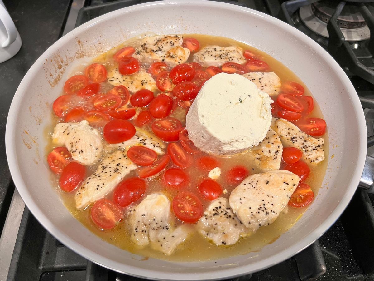 Boursin garlic herb cheese added to a skillet with chicken chunks, halves grape tomatoes and chicken broth.