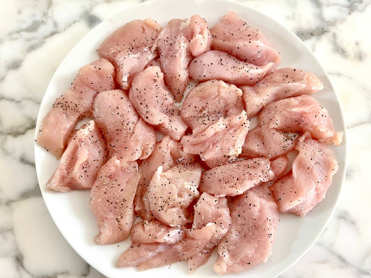 Raw chicken breast chunks seasoned in a bowl.