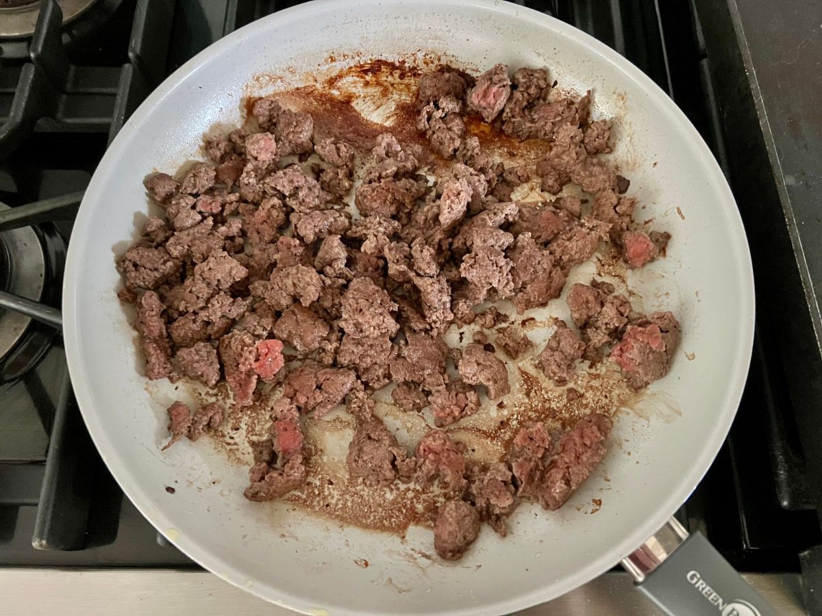 Ground beef sauteing in a skillet with garlic and salt, pepper.