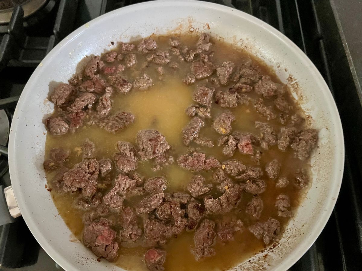 Chicken base and pasta water added to the ground beef mixture in a skillet.