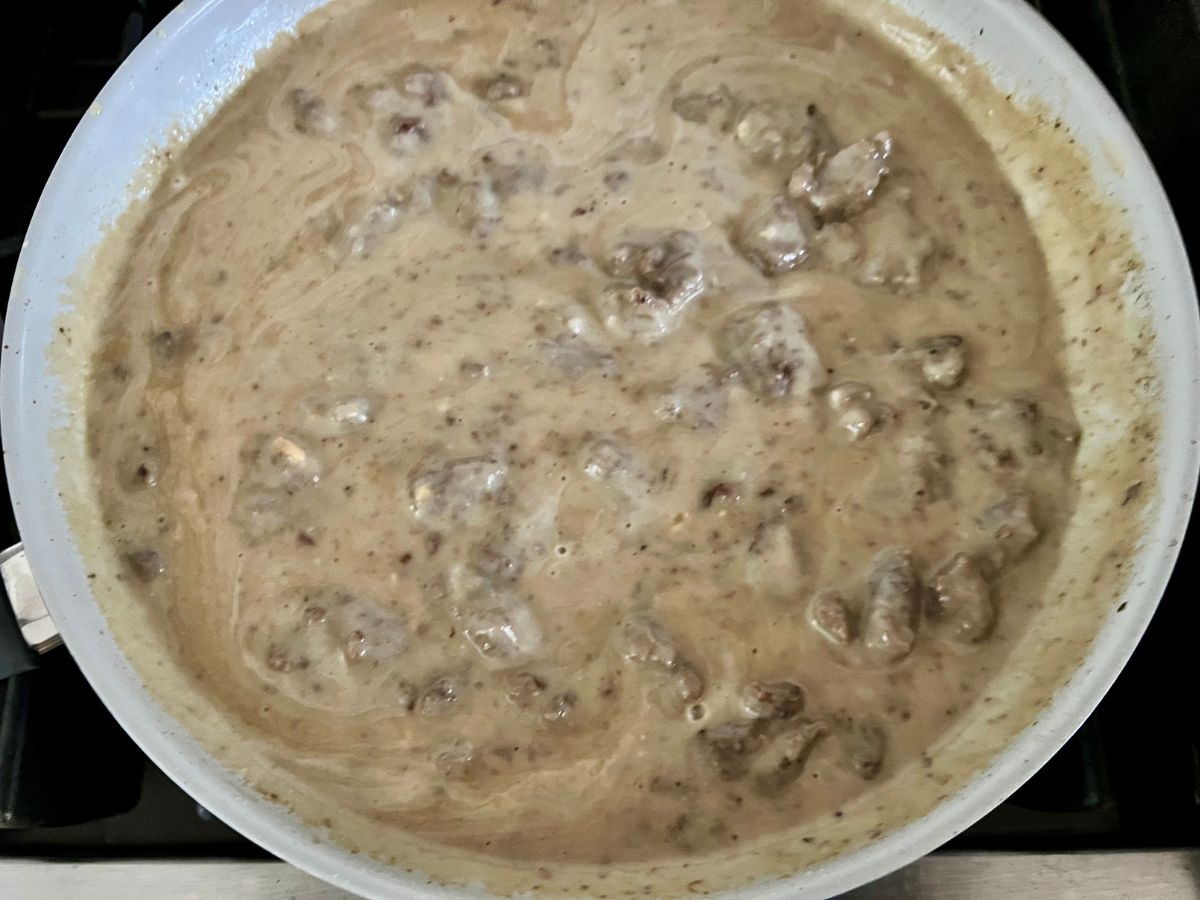 Alfredo sauce with ground beef thickening in a skillet.