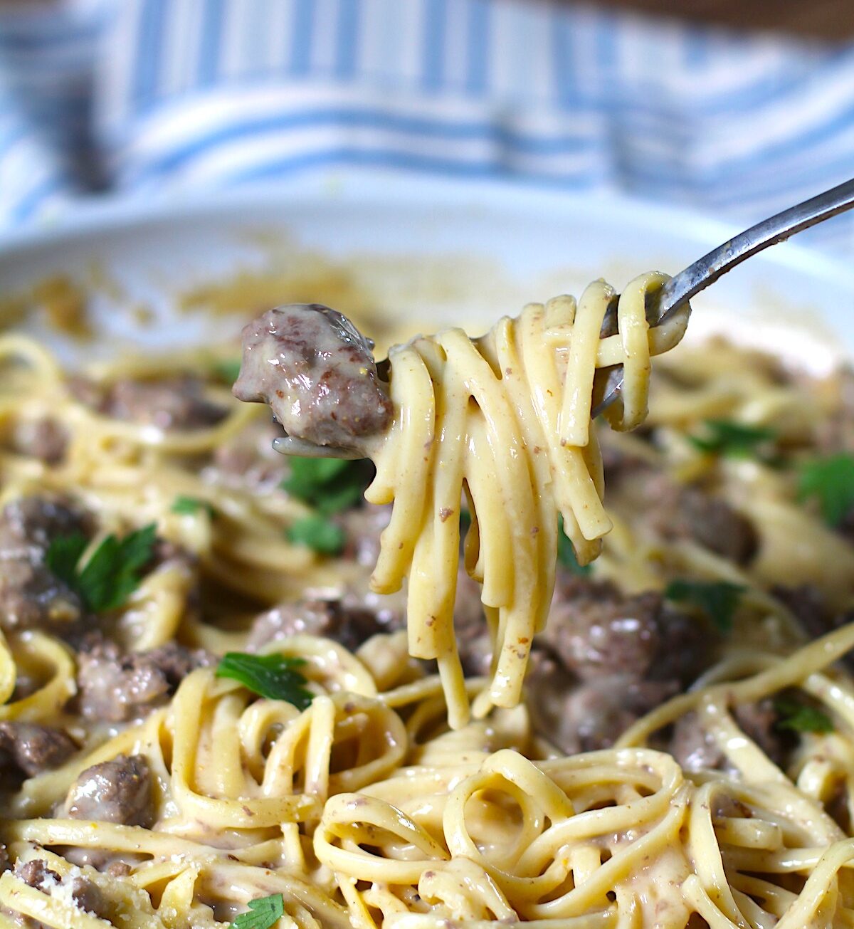Creamy Alfredo Ground Beef Pasta with fettuccine pasta and parsley on top in a skillet on a wood table with blue and white towel.