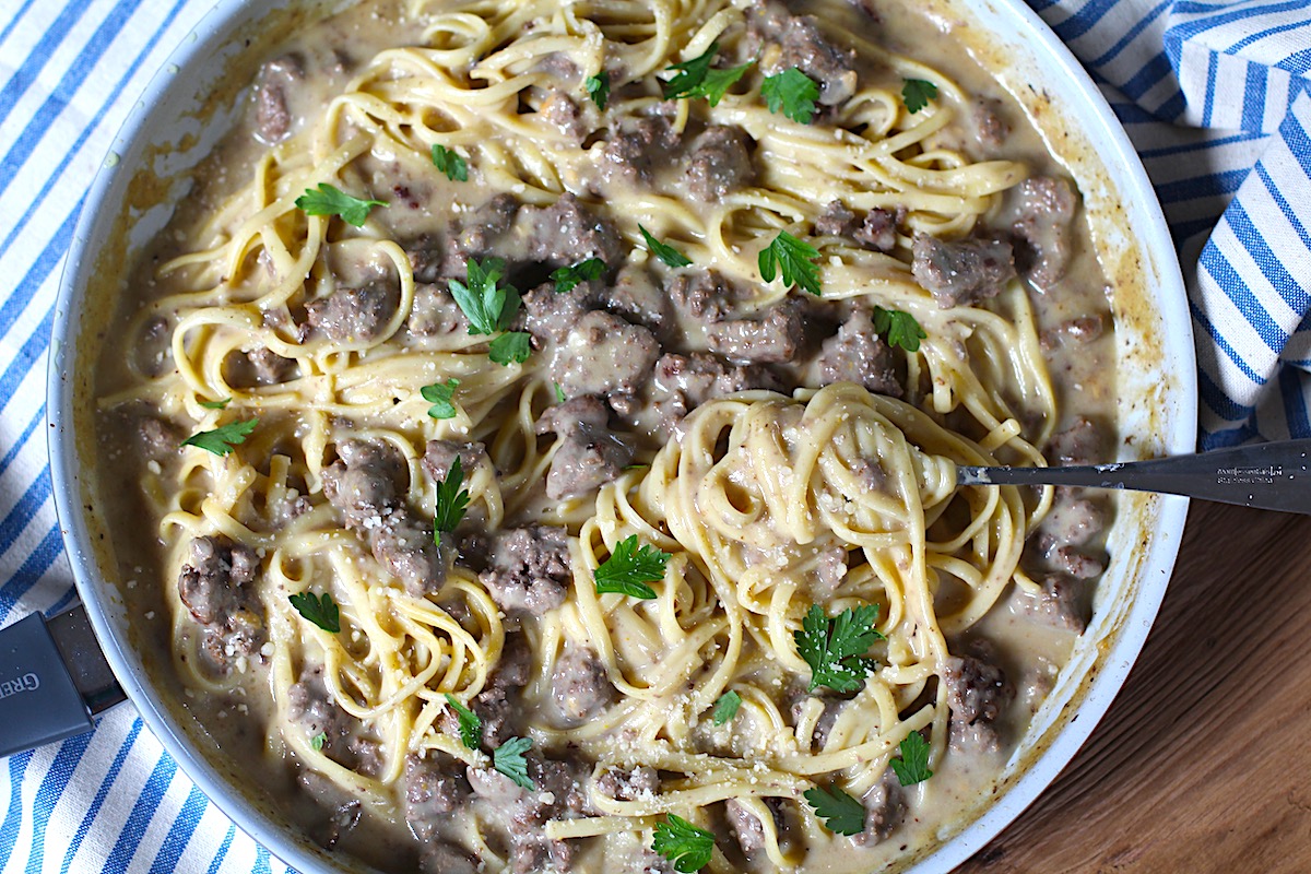 Creamy Alfredo Ground Beef Pasta with fettuccine pasta and parsley on top in a skillet on a wood table with blue and white towel.