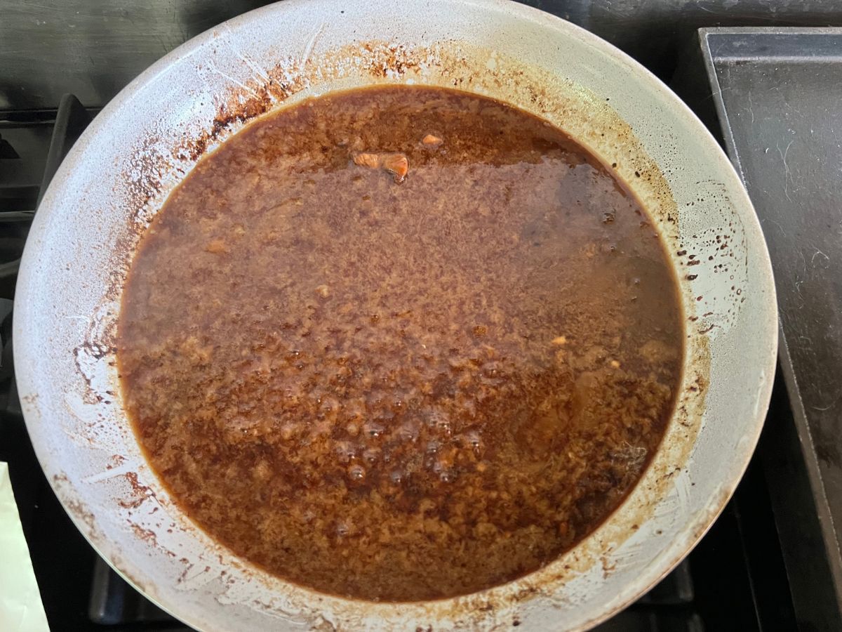 Honey ginger sauce poured over chicken breast chunks in a skillet to simmering for honey ginger chicken.