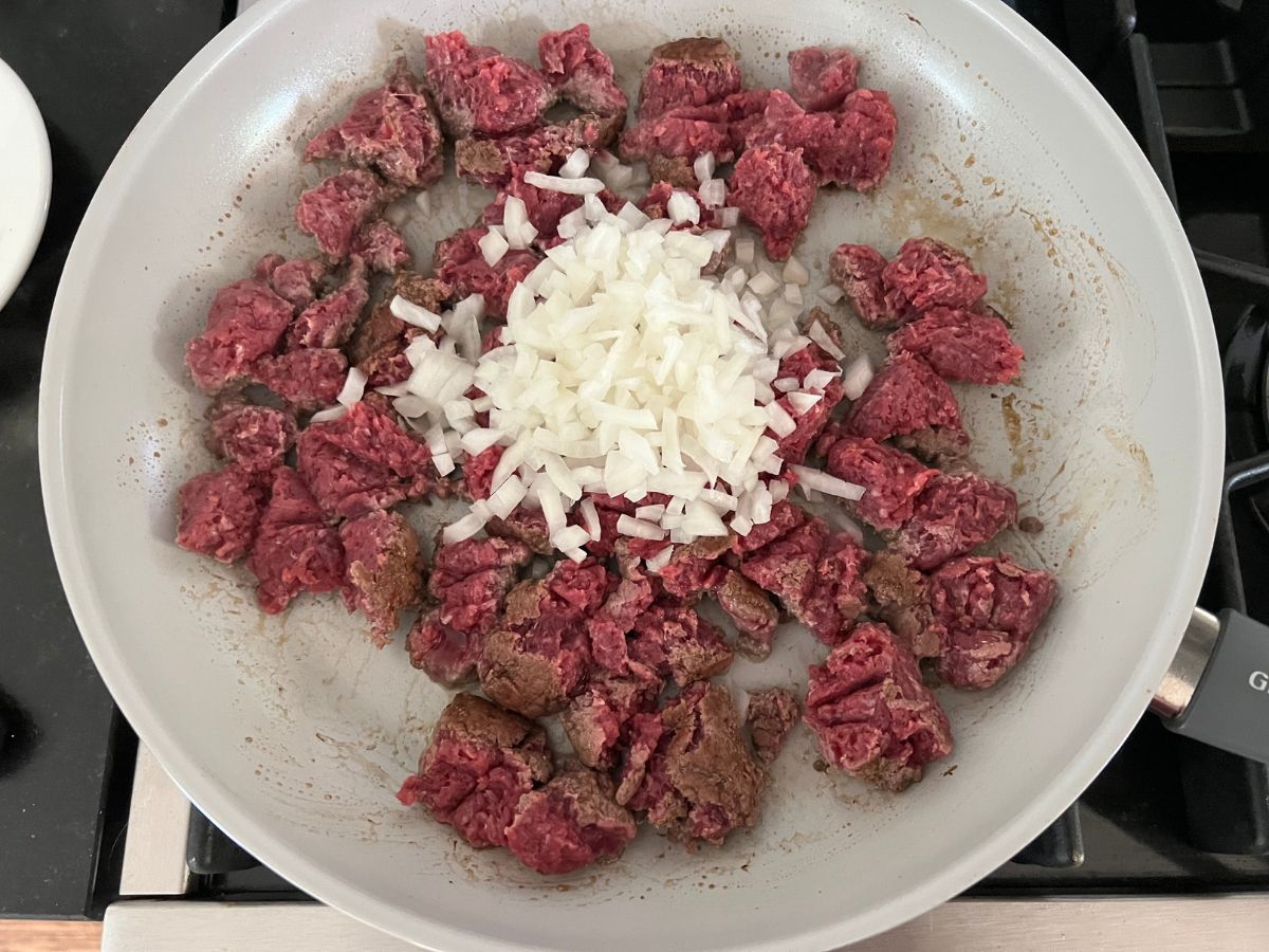 Ground beef and diced onions added to a skillet.