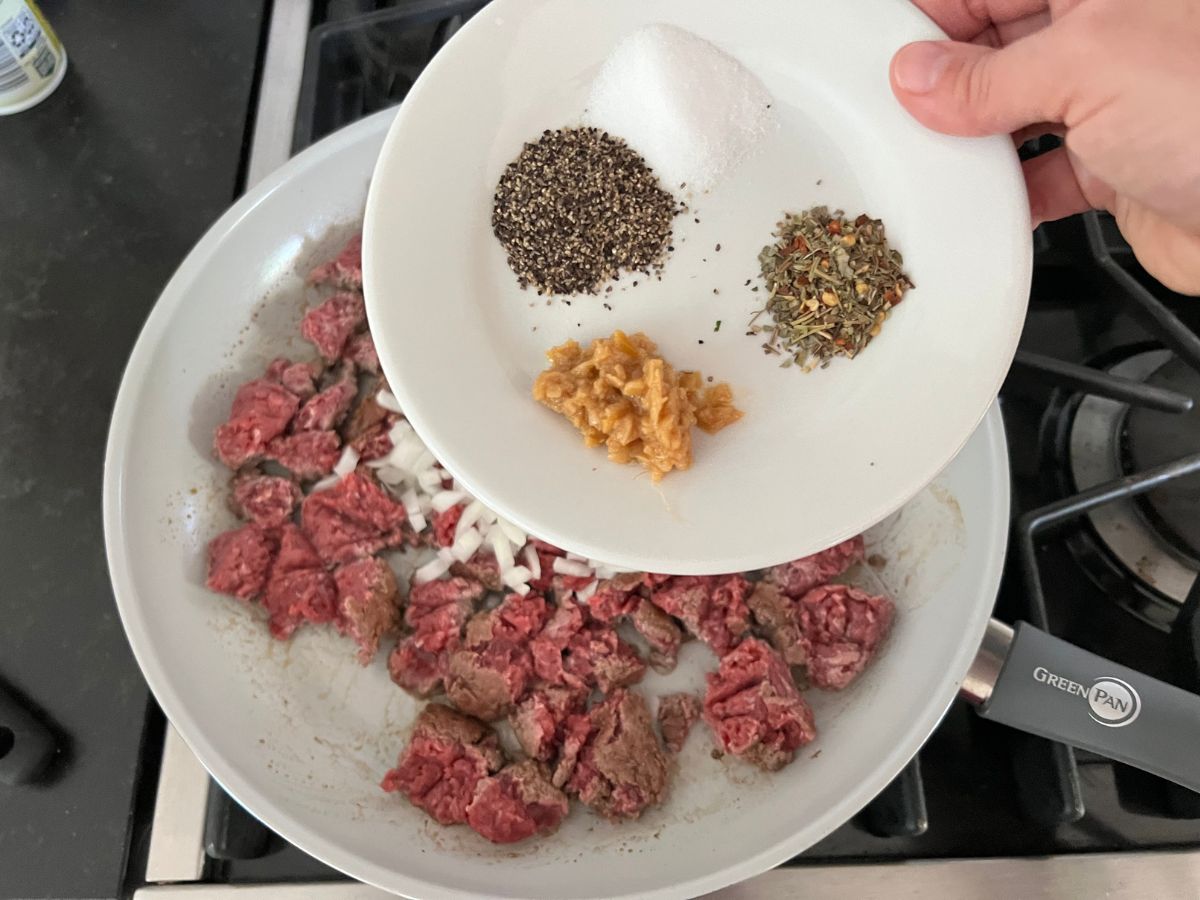 Seasonings measured out onto a plate being poured into the ground beef mixture.