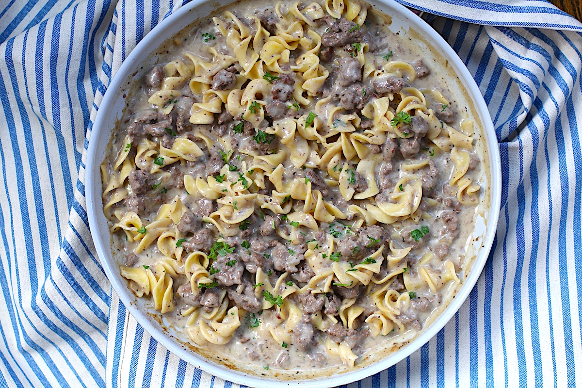 Creamy Beef and Noodles with ground beef and parsley garnish in a skillet on table on blue and white striped towel.