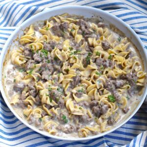 Creamy Beef and Noodles with ground beef and parsley garnish in a skillet on table on blue and white striped towel.