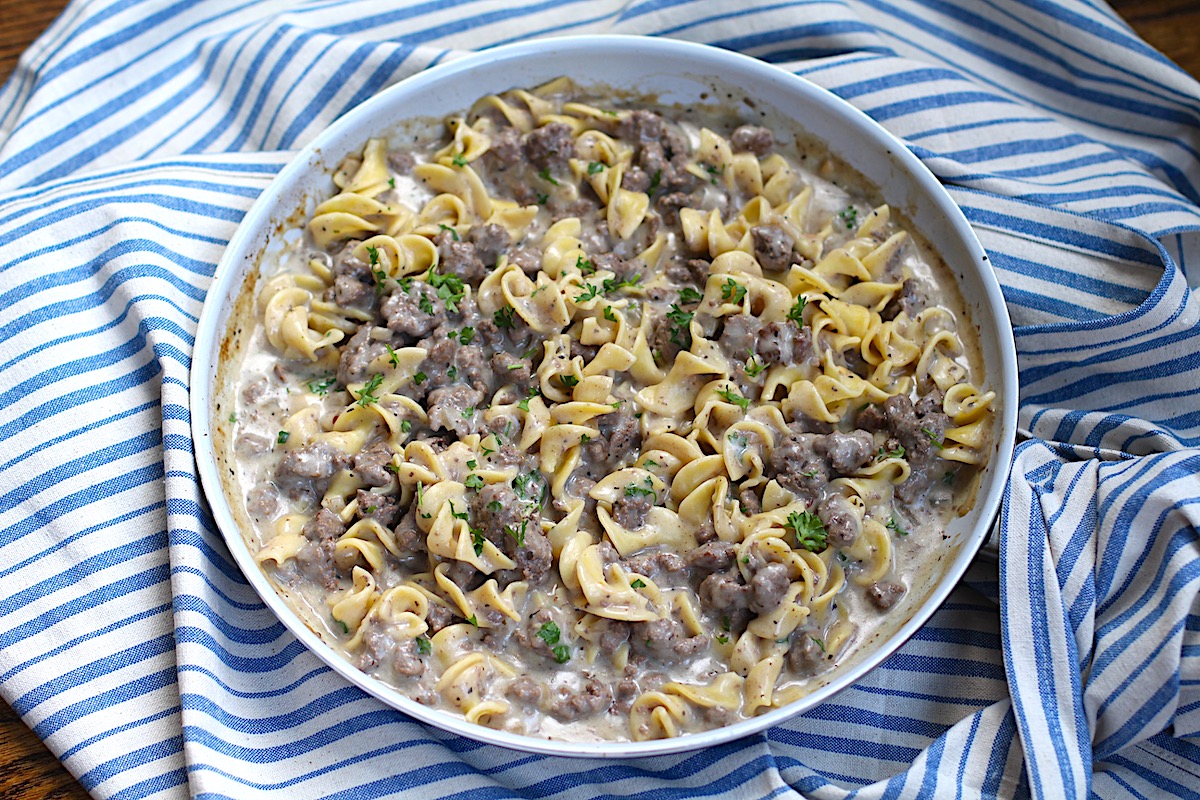 Creamy Beef and Noodles with ground beef and parsley garnish in a skillet on table on blue and white striped towel.