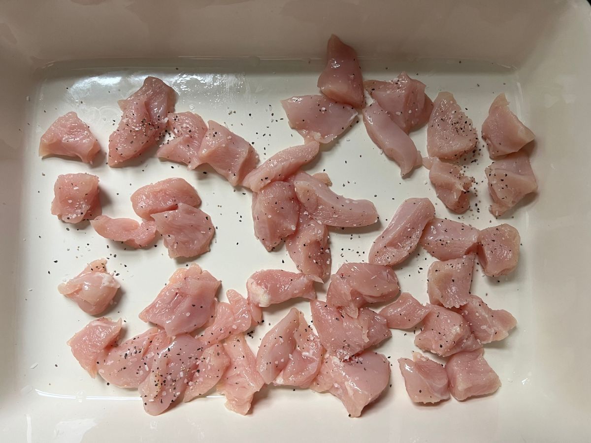 Diced chicken breast pieces in a baking dish sprinkled with salt and pepper.