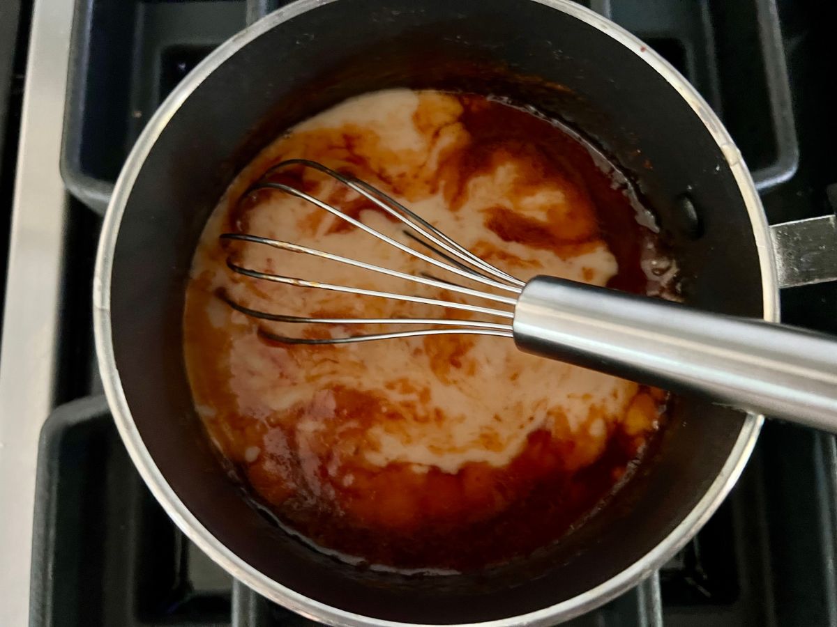 Whisk in a saucepan with cornstarch slurry being combined as it simmers.