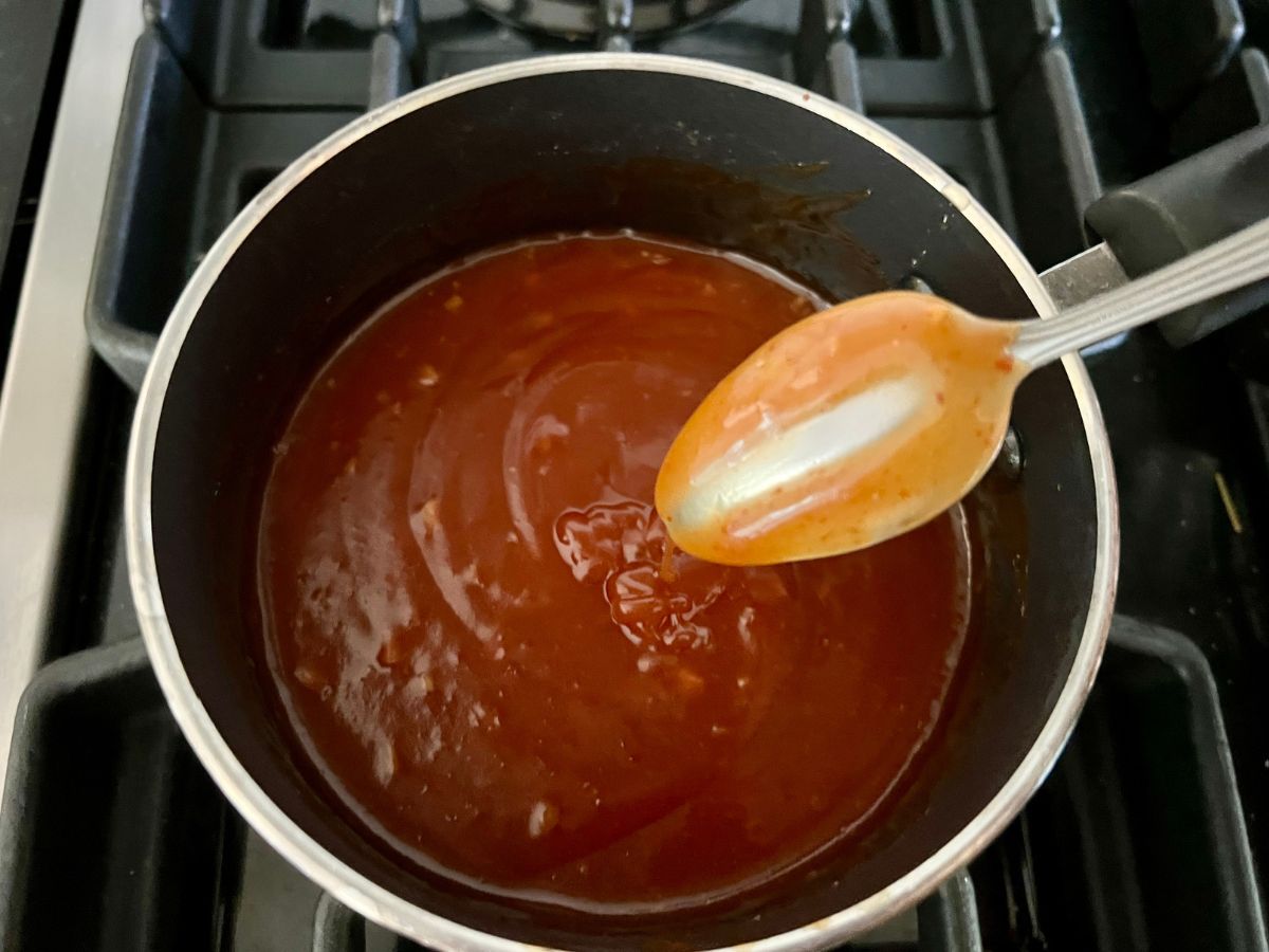 The back of a spoon coated in the thickened and ready to serve honey sriracha sauce over the saucepan.