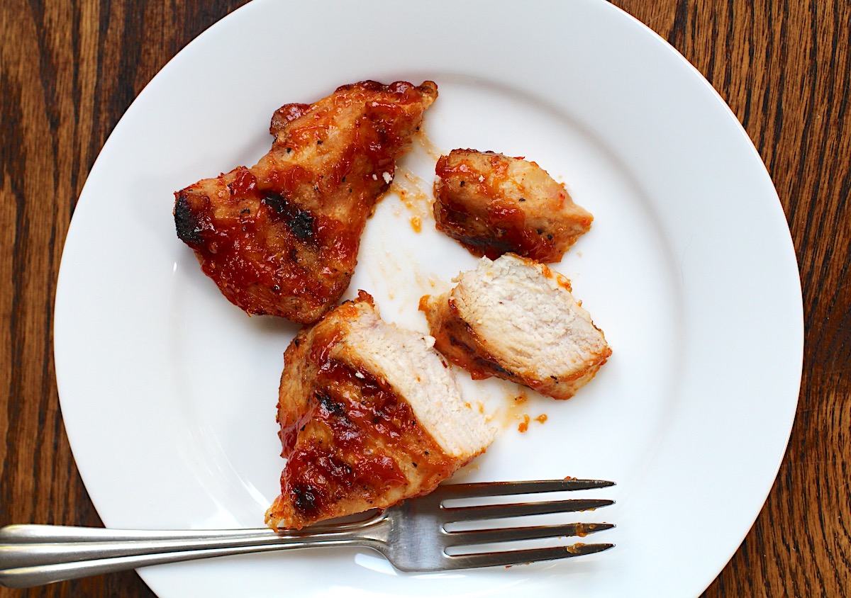 Honey Sriracha Sauce coated chicken breast sliced on a plate on wood table.